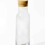Glass jug with a cork lid, adorned with white Arabic alphabets designed in an array of dots.